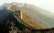 A section of the Great Wall of China stretches across a mountainous landscape, featuring a series of watchtowers connected by a stone pathway. The wall winds through barren trees and the scene is enveloped in a misty atmosphere, creating a sense of depth and history.