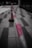A close-up view of a red and white striped barrier tape stretched across a tiled floor, with the focus primarily on the tape. In the background, a blurred traffic cone is visible.