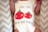 A baby is wearing a white onesie featuring a playful design of two smiling red tomatoes with green leaves. Above and below the tomatoes, there is a humorous phrase: 'I love you from my head to-ma-toes.' The background consists of a soft zigzag patterned fabric.