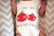 A baby is wearing a white onesie featuring a playful design of two smiling red tomatoes with green leaves. Above and below the tomatoes, there is a humorous phrase: 'I love you from my head to-ma-toes.' The background consists of a soft zigzag patterned fabric.