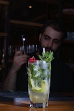 A vibrant cocktail with tequila garnished with fresh lime and herbs on a wooden table.