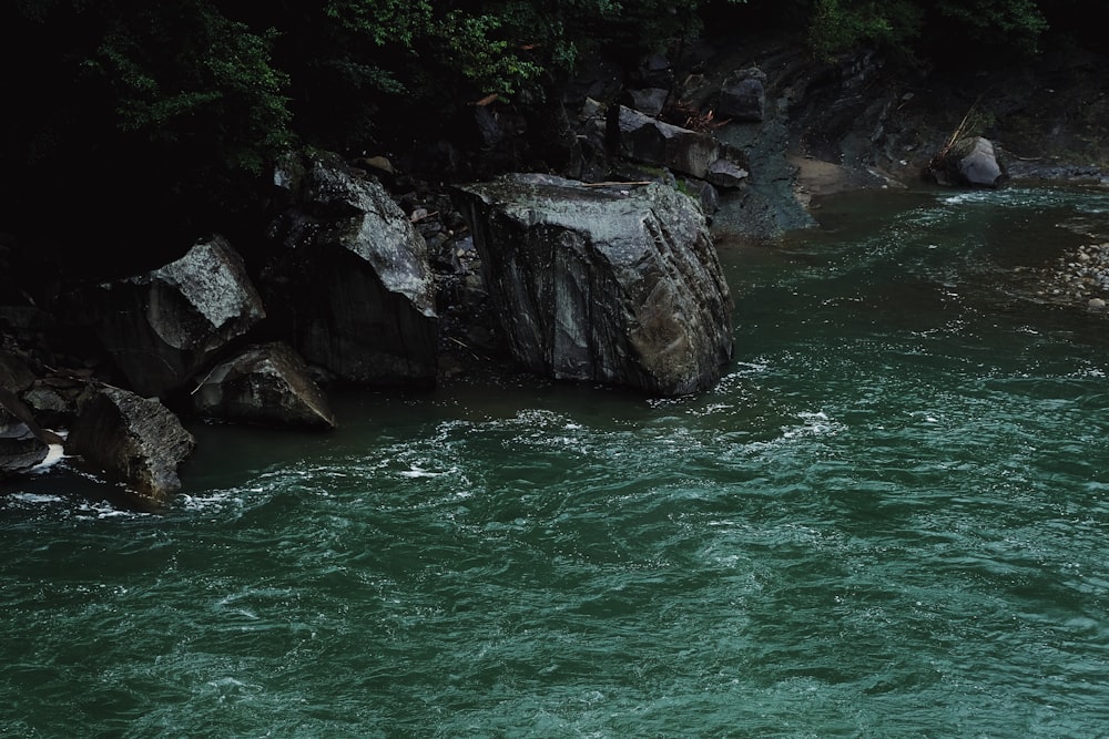 green body of water near gray rocky mountain during daytime