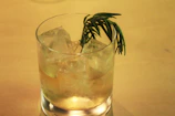 Hand pouring a sparkling cocktail into a tall glass with ice and a sprig of rosemary.