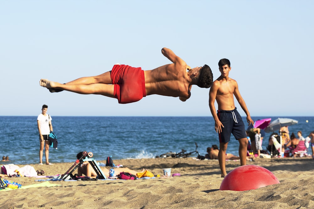 homme en short rouge assis sur une chaise en plastique rouge sur la plage pendant la journée