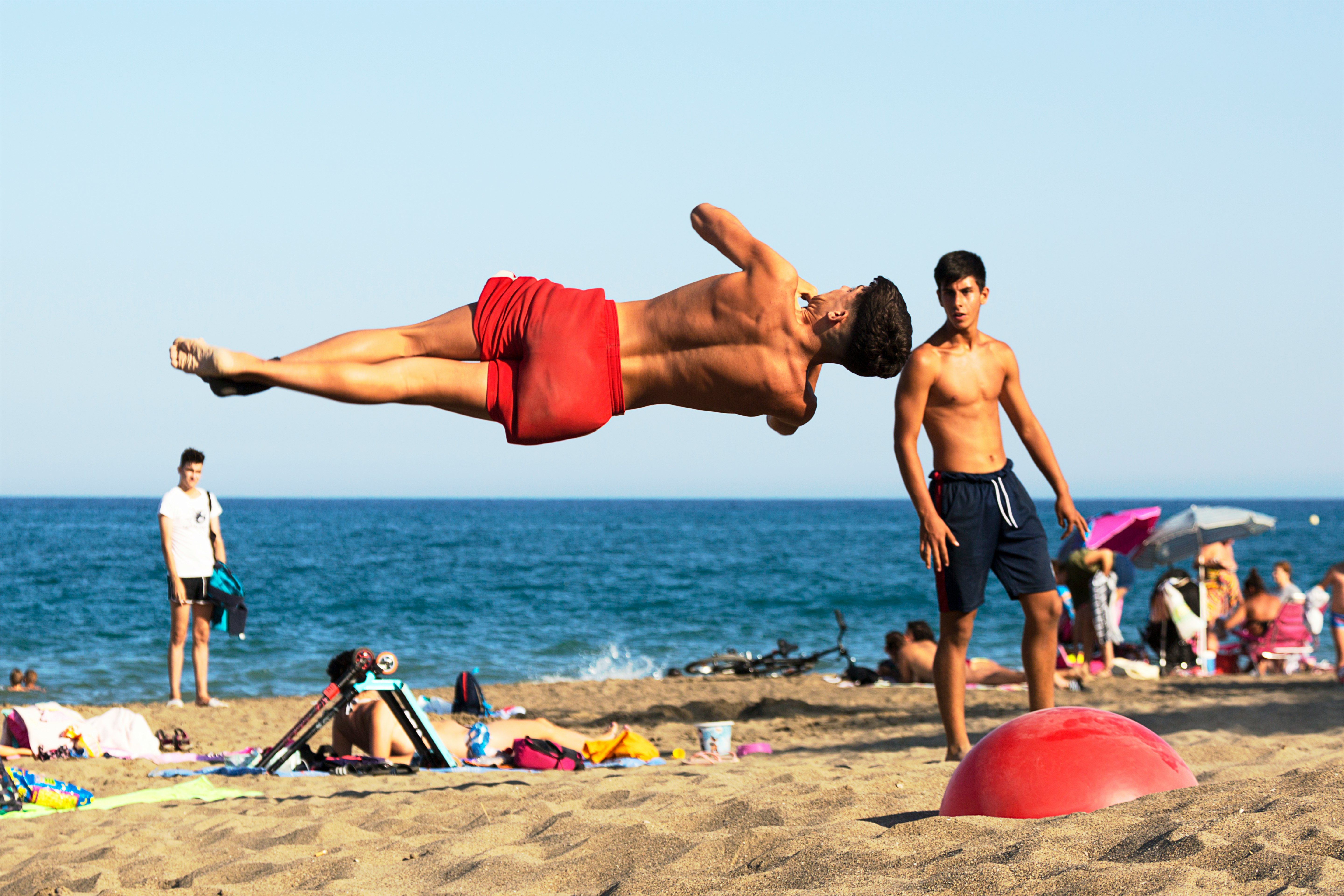 man in red shorts sitting on red plastic chair on beach during daytime