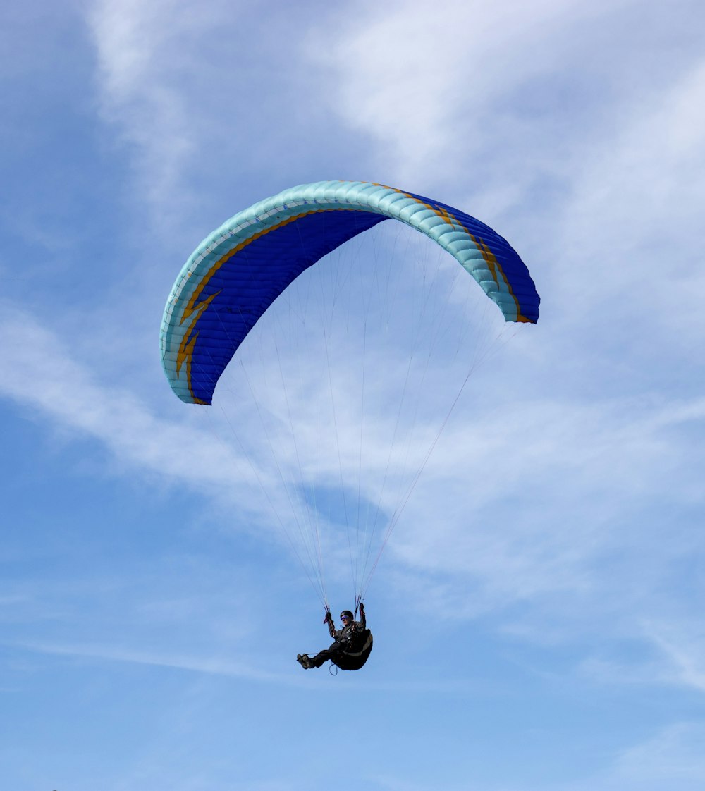 person riding on yellow and blue parachute under blue sky during daytime