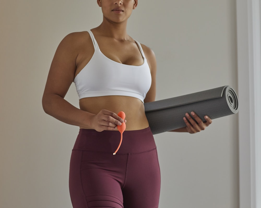 woman in white sports bra and purple leggings holding black speaker