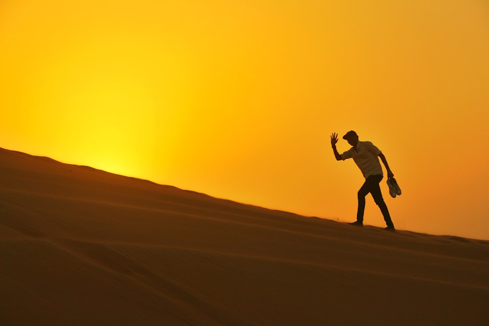Silhouette eines Mannes, der während des Sonnenuntergangs durch die Wüste geht