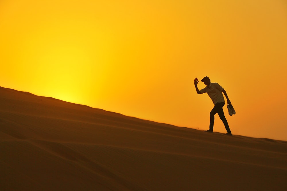 silhouette dell'uomo che cammina sul deserto durante il tramonto