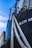 Detailed view of a ship with a close-up of its ropes and part of its hull. The ship's name is partially visible in bold white letters. The sky is blue with some clouds, and a cargo container is partially seen in the background.