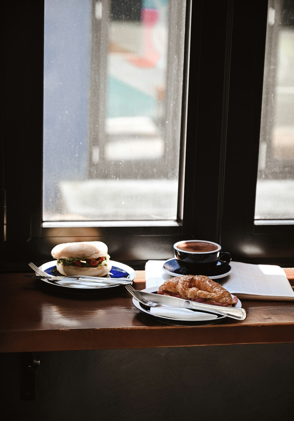 갈색 나무 테이블에 검은 세라믹 머그잔 옆에 흰색 세라믹 접시에 햄버거