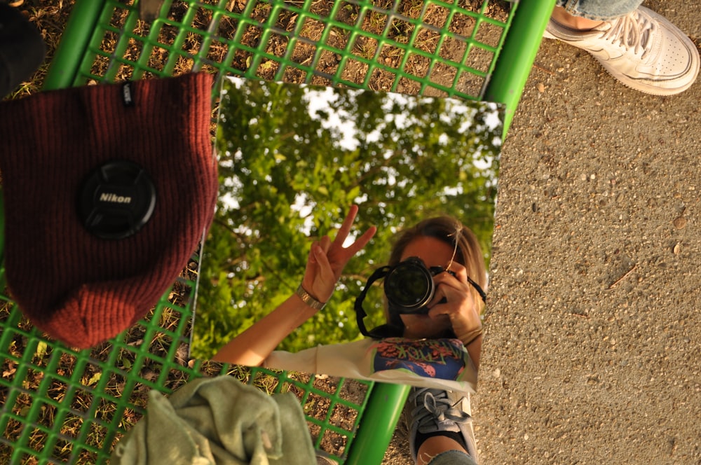 woman in green shirt wearing black sunglasses sitting on green metal bench during daytime