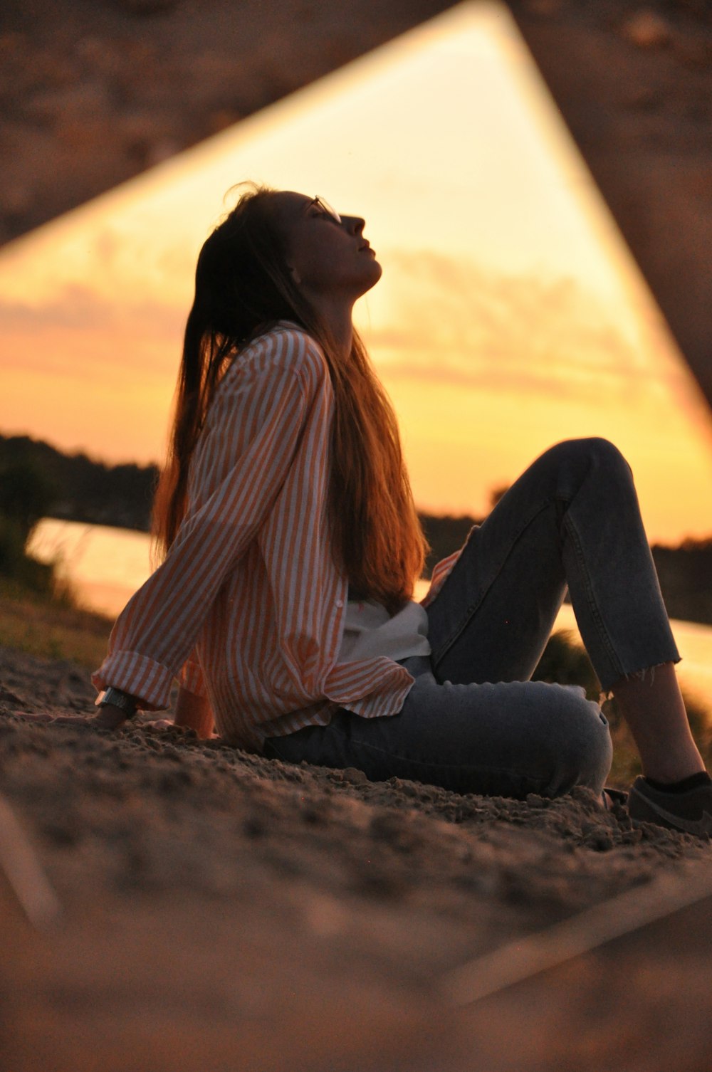 woman in white and brown striped long sleeve shirt and blue denim jeans sitting on brown