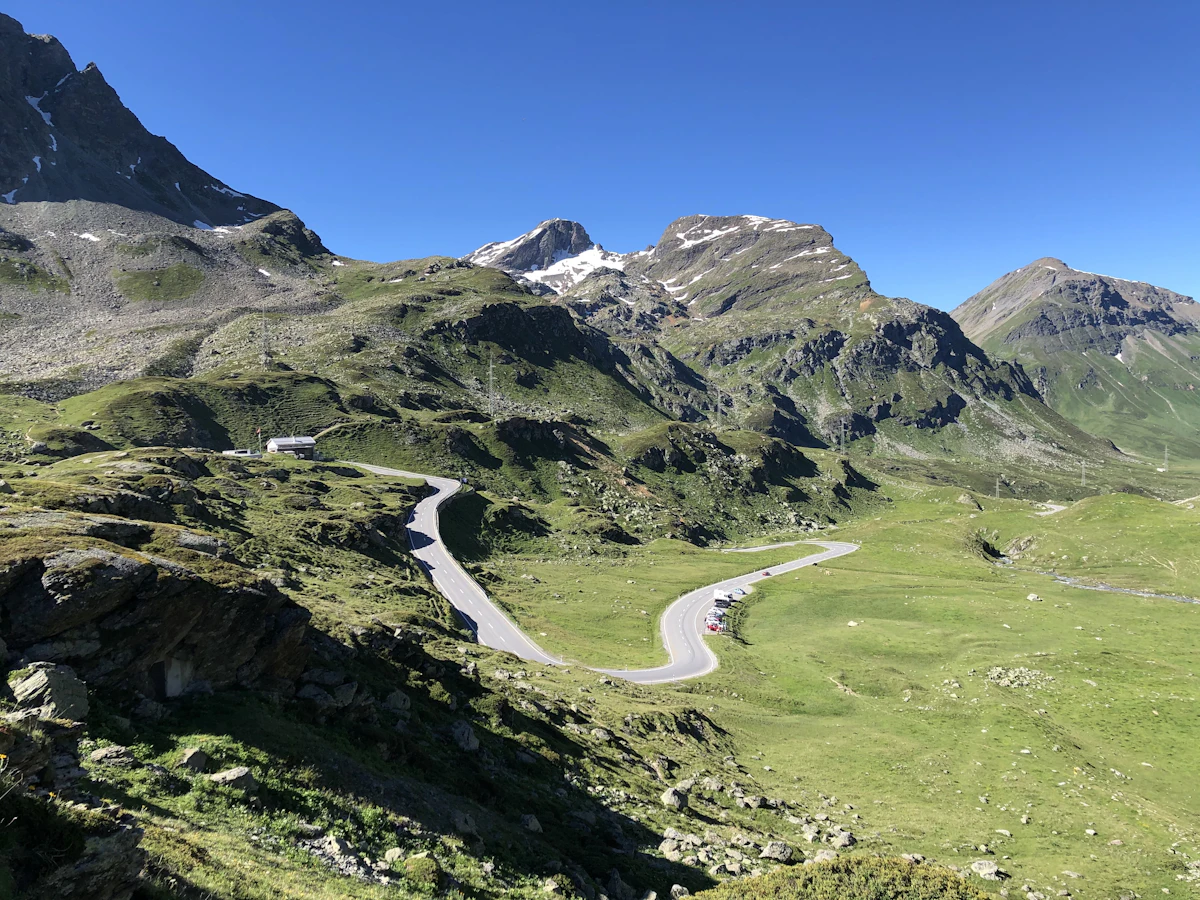 The road up to the Julier Pass winding through green alpine meadows below snow-streaked peaks