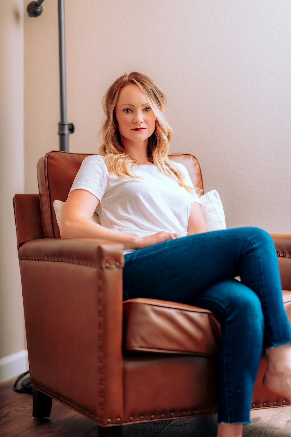 woman in white shirt and blue denim jeans sitting on brown leather armchair