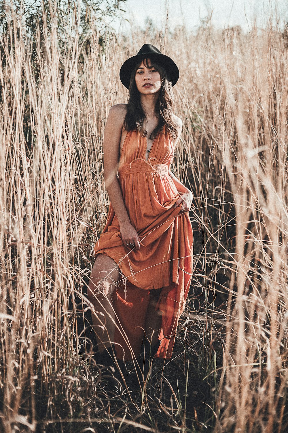 woman in orange sleeveless dress standing on brown grass field during daytime
