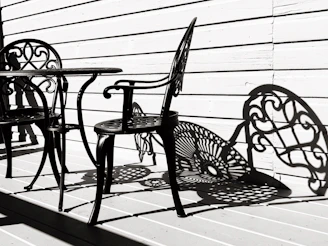 An elegant wrought iron outdoor bar table with two matching stools, placed on a stone patio at sunset.