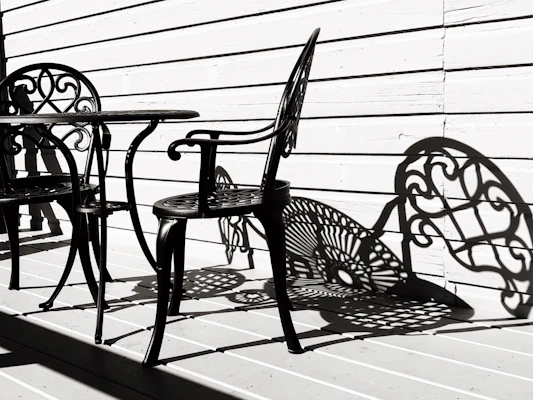 An elegant wrought iron outdoor bar table with two matching stools, placed on a stone patio at sunset.