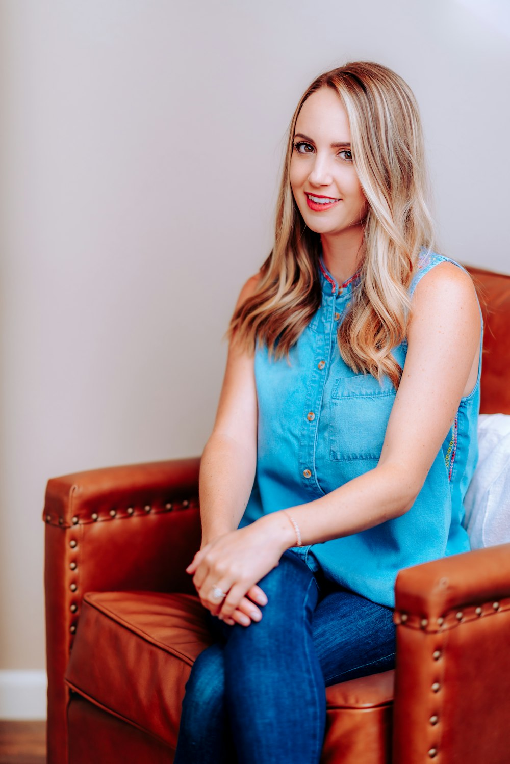 woman in blue sleeveless dress sitting on brown leather armchair