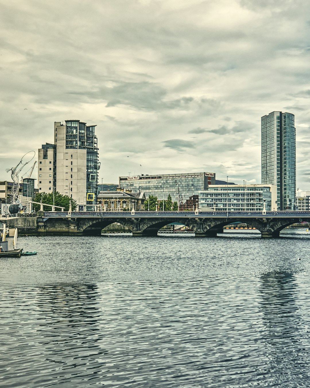 Looking down the River Lagan toward Queens Bridge; featuring, from left to right, Beacon of Hope Statue, the Ships Building, Custom House, Royal Mail Building, and the Obel Building in the Cathedral Quarter (Jul., 2020).