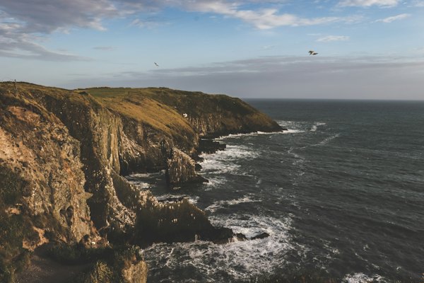 Brown rock formation beside sea under blue sky during daytime — Cork & Kinsale, Ireland