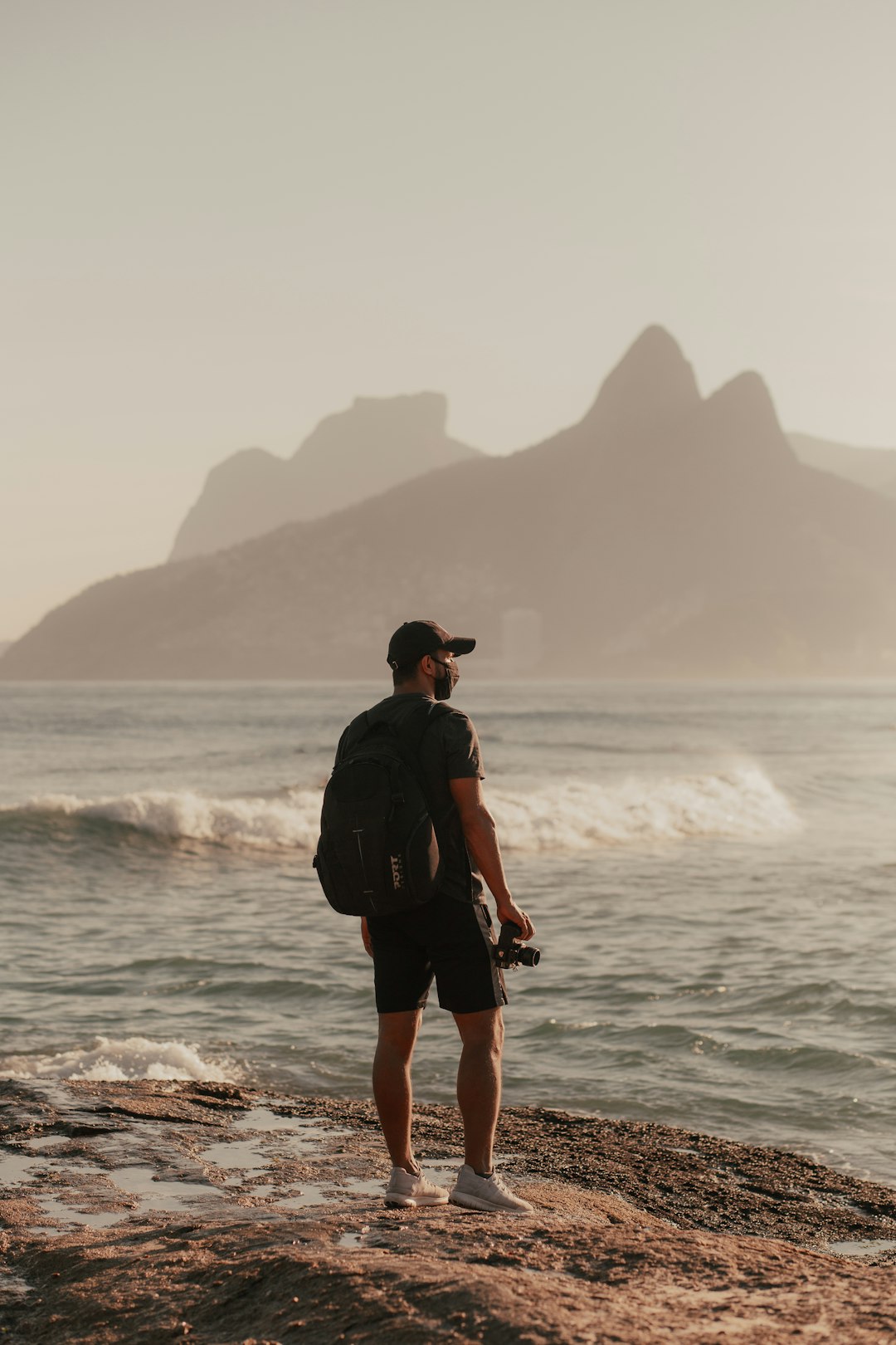 man in black t-shirt and black shorts standing on rocky shore during daytime