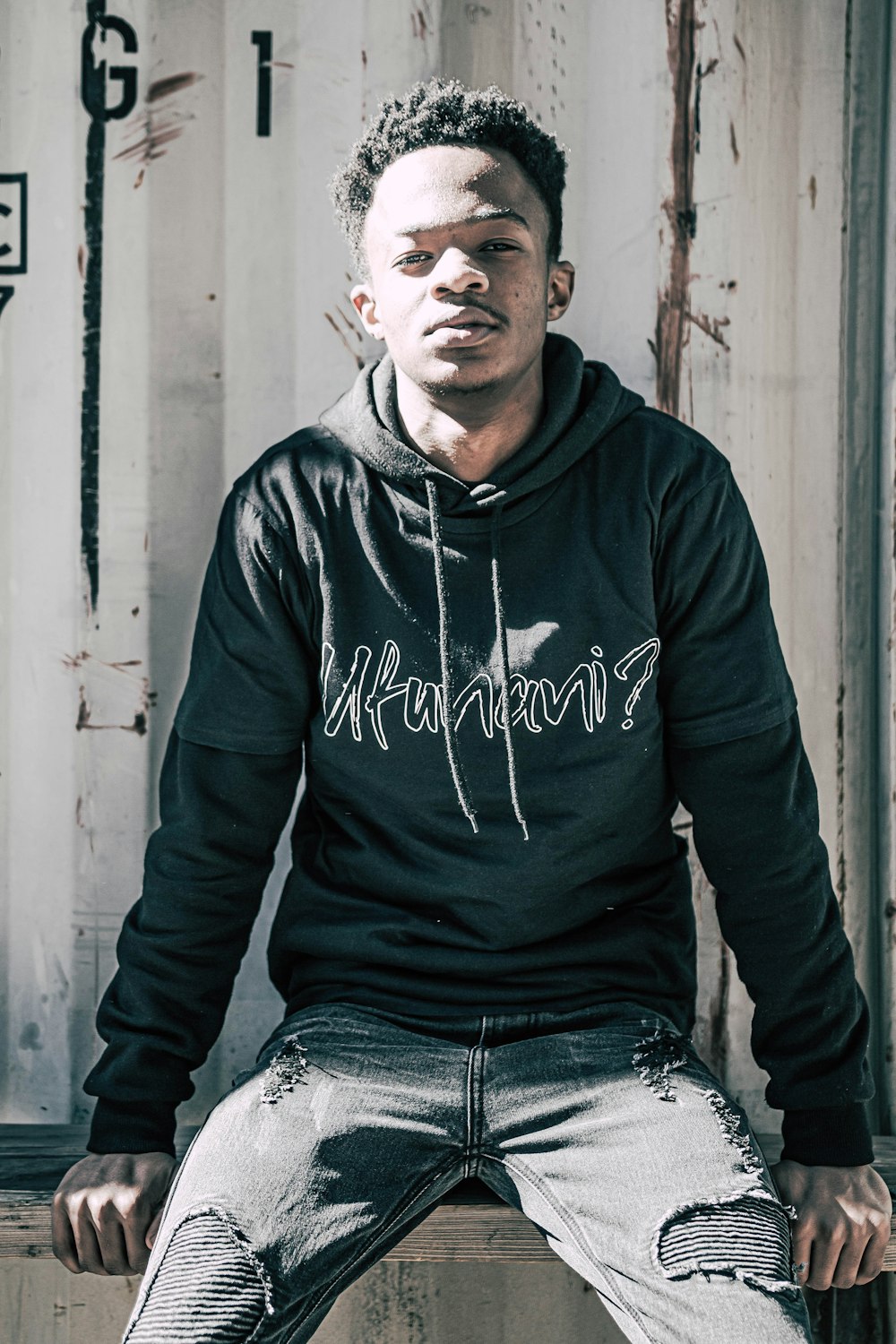 man in black nike hoodie and blue denim jeans sitting on white wooden bench