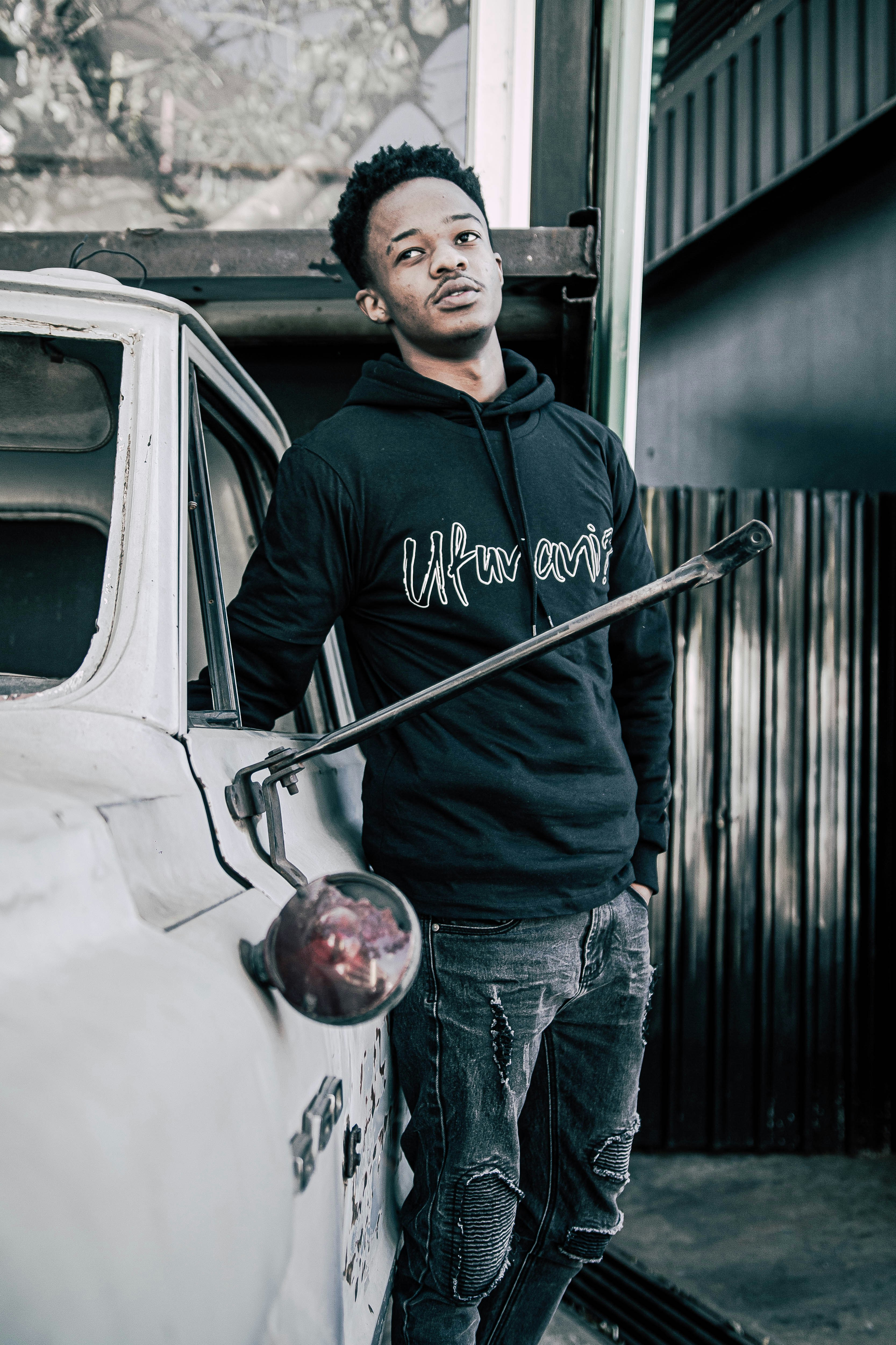 homem em preto e branco moletom pullover e jeans azul de pé ao lado do carro branco