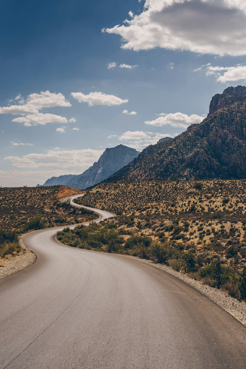 gray asphalt road between green trees and brown mountains during daytime