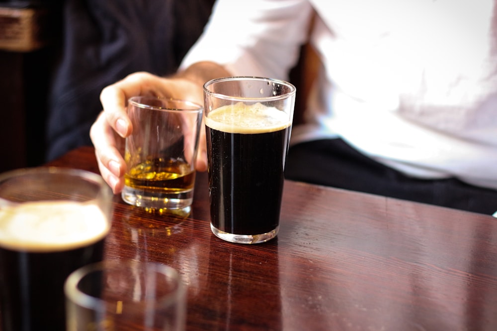 person holding clear drinking glass with black liquid