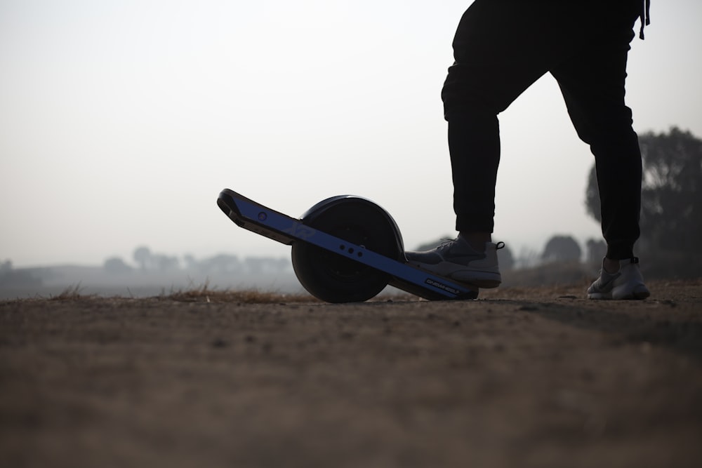 Persona in giacca e pantaloni neri in piedi sullo skateboard blu durante il giorno