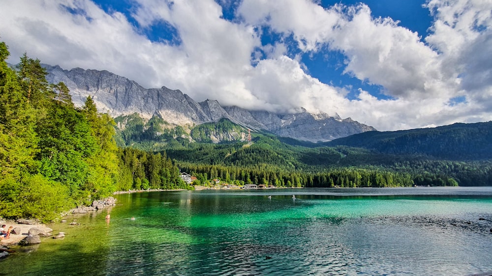 alberi verdi vicino al lago e alla montagna sotto il cielo nuvoloso blu e bianco durante il giorno