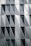 A modern building facade featuring a geometric pattern composed of triangular and rectangular panels. The surface alternates between translucent and opaque materials, and the structure exhibits a sleek, minimalist design. Windows are uniformly distributed across the grid-like pattern.