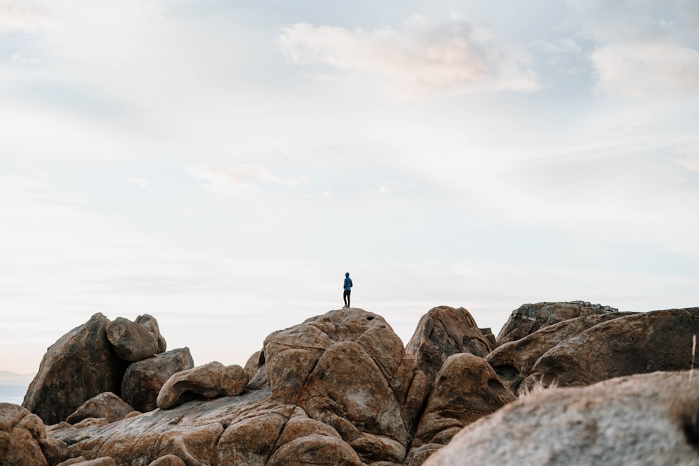 person standing on brown rock formation under white clouds during daytime