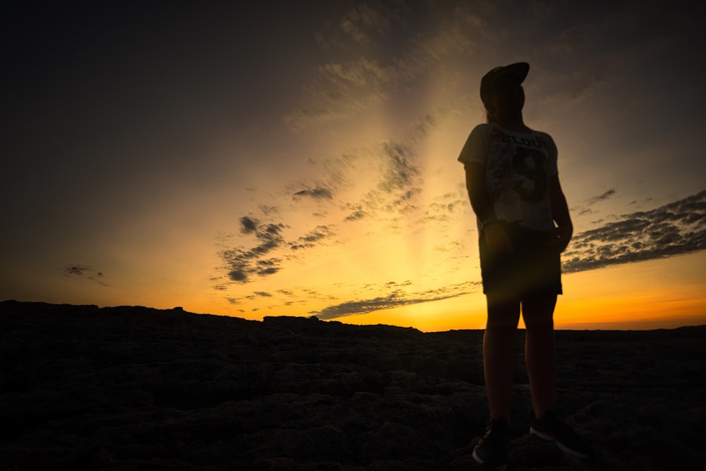 woman in white tank top and black shorts standing on brown sand during sunset