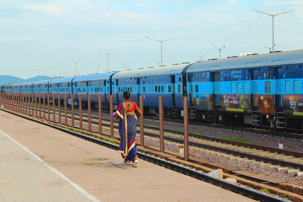 man in blue and white striped shirt standing beside blue train during daytime