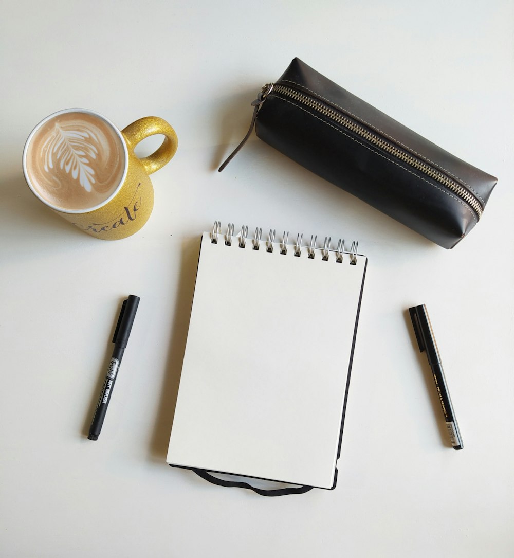 white ceramic mug beside black pen and white notebook