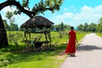 woman in red dress walking on pathway near brown wooden gazebo during daytime