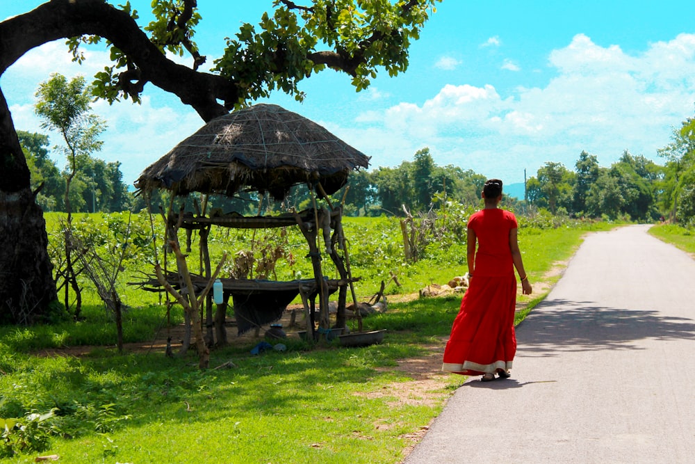 woman in red dress walking on pathway near brown wooden gazebo during daytime