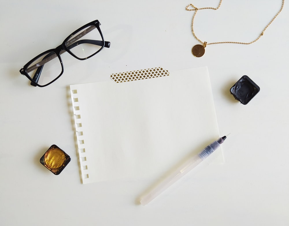 black framed eyeglasses beside black ceramic mug and white pen on white printer paper