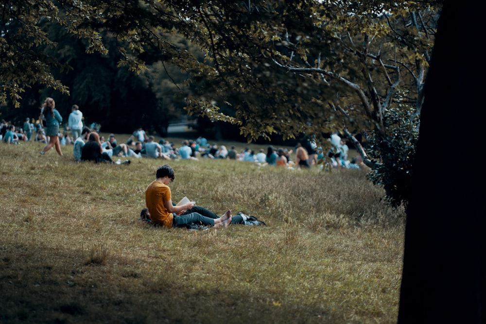 man in orange t-shirt sitting on green grass field during daytime