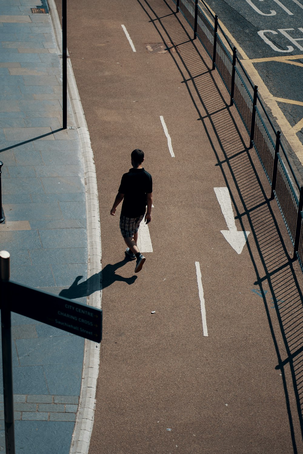 uomo in t-shirt nera e jeans blu denim che cammina sul marciapiede di cemento grigio durante il giorno