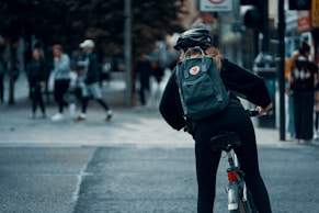 person in black jacket and black pants with green backpack riding on black motorcycle during daytime