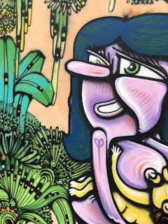 A colorful graffiti piece featuring a stylized cartoonish character with exaggerated facial features and long blue hair. The character has a playful expression and is surrounded by vibrant, abstract jungle-like foliage.