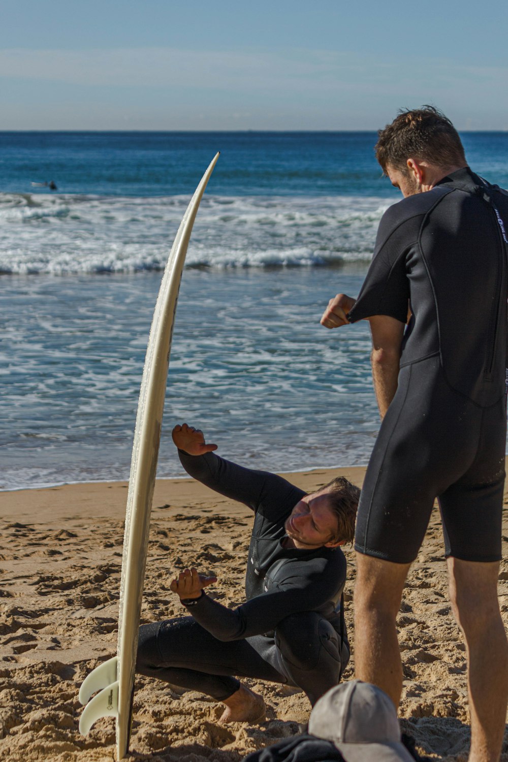 a man in a wet suit standing next to a surfboard