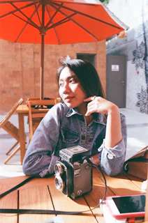 A warm, candid photo of a sunlit outdoor workspace with a camera and notebook resting on a wooden table.