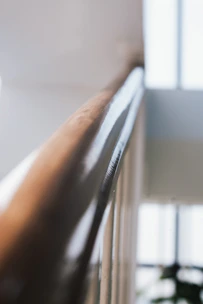 Close-up of hands wiping a shiny handrail with a cloth in a well-lit hallway.