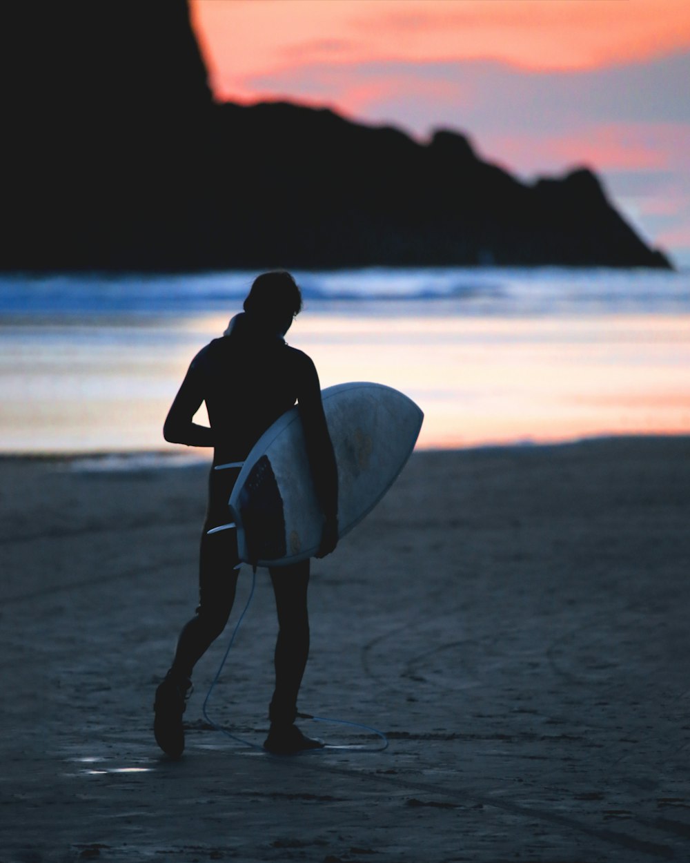 silhouette of woman holding surfboard walking on beach during sunset