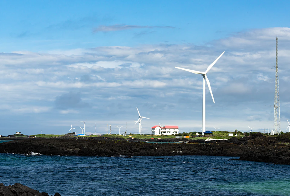 Wind turbines stand tall on rocky shoreline with spinning blades amidst clear blue sky