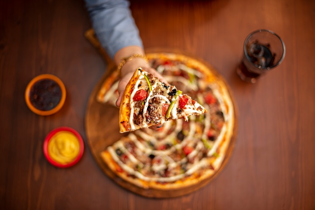 person holding pizza with cheese and red sauce